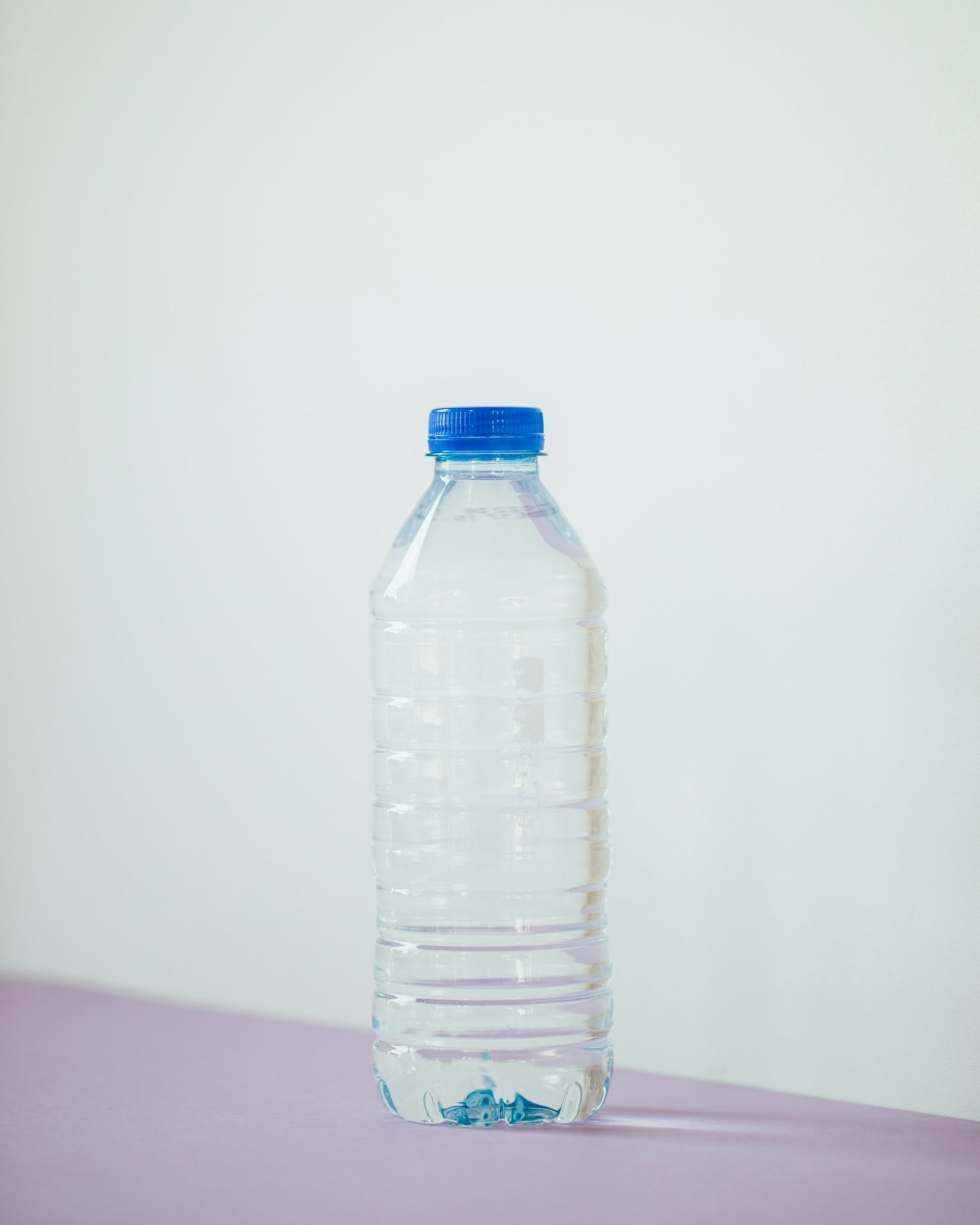 Clear plastic water bottle standing on a white surface against a pale blue background
