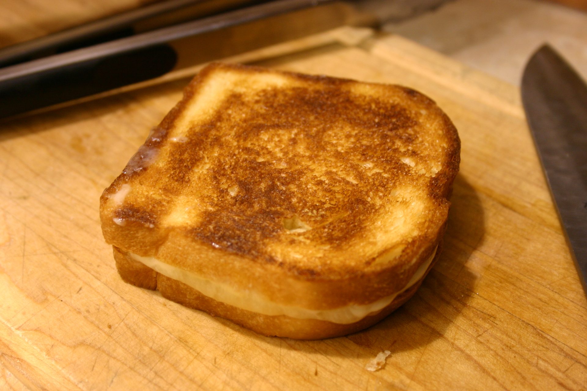 A golden-brown grilled cheese sandwich on a wooden cutting board, with melted cheese visible between the slices.