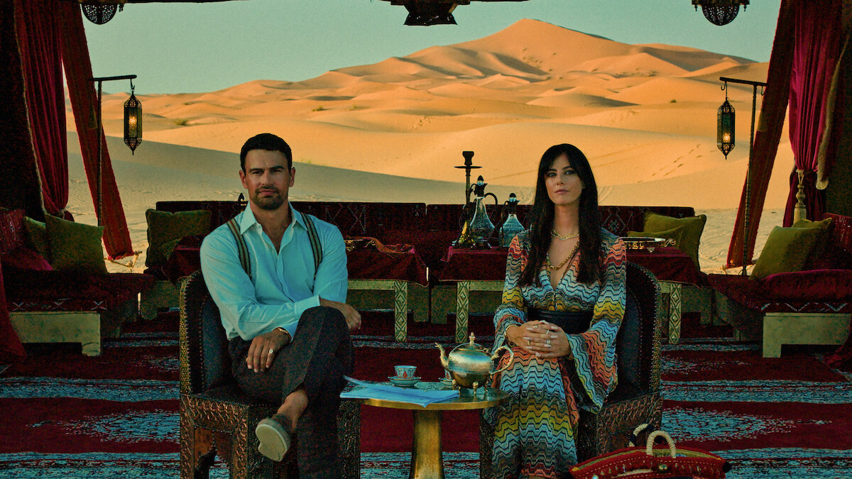 Two people sit in an ornate desert tent with a tea service.